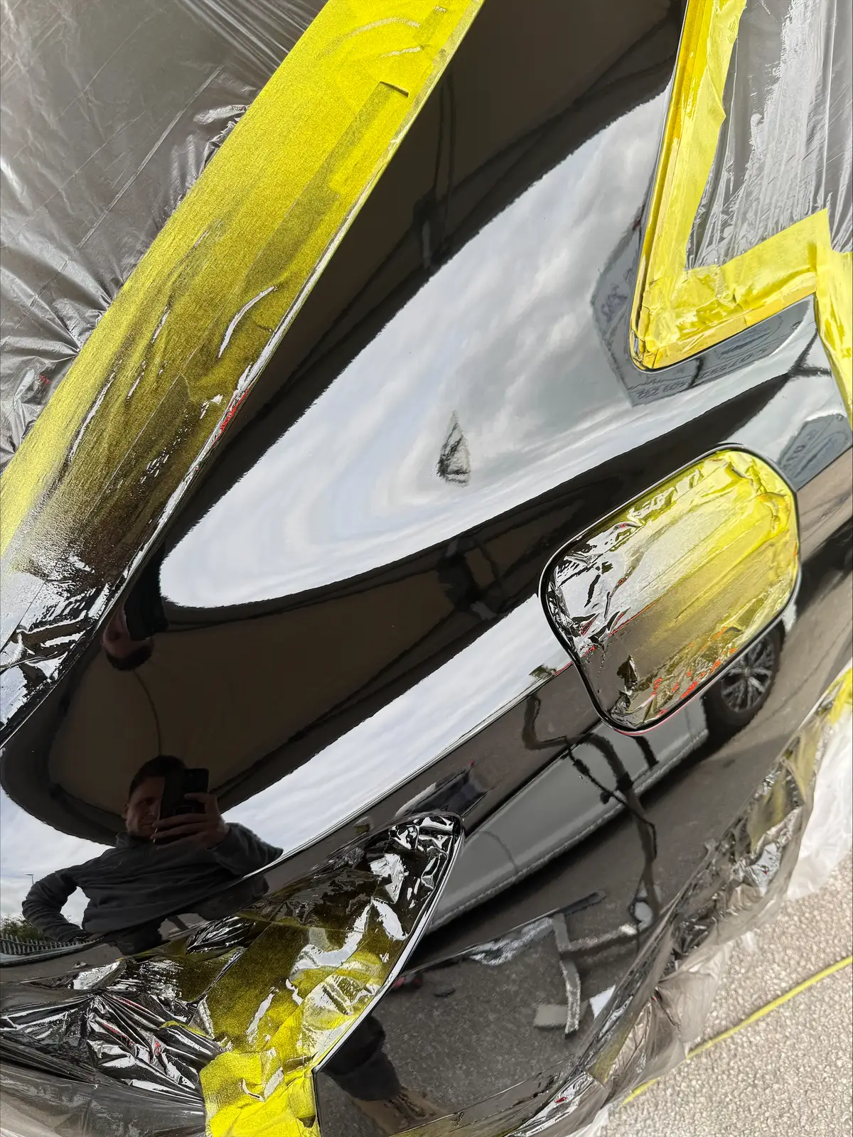 Black car rear quarter panel during dent repair, masked for refinishing