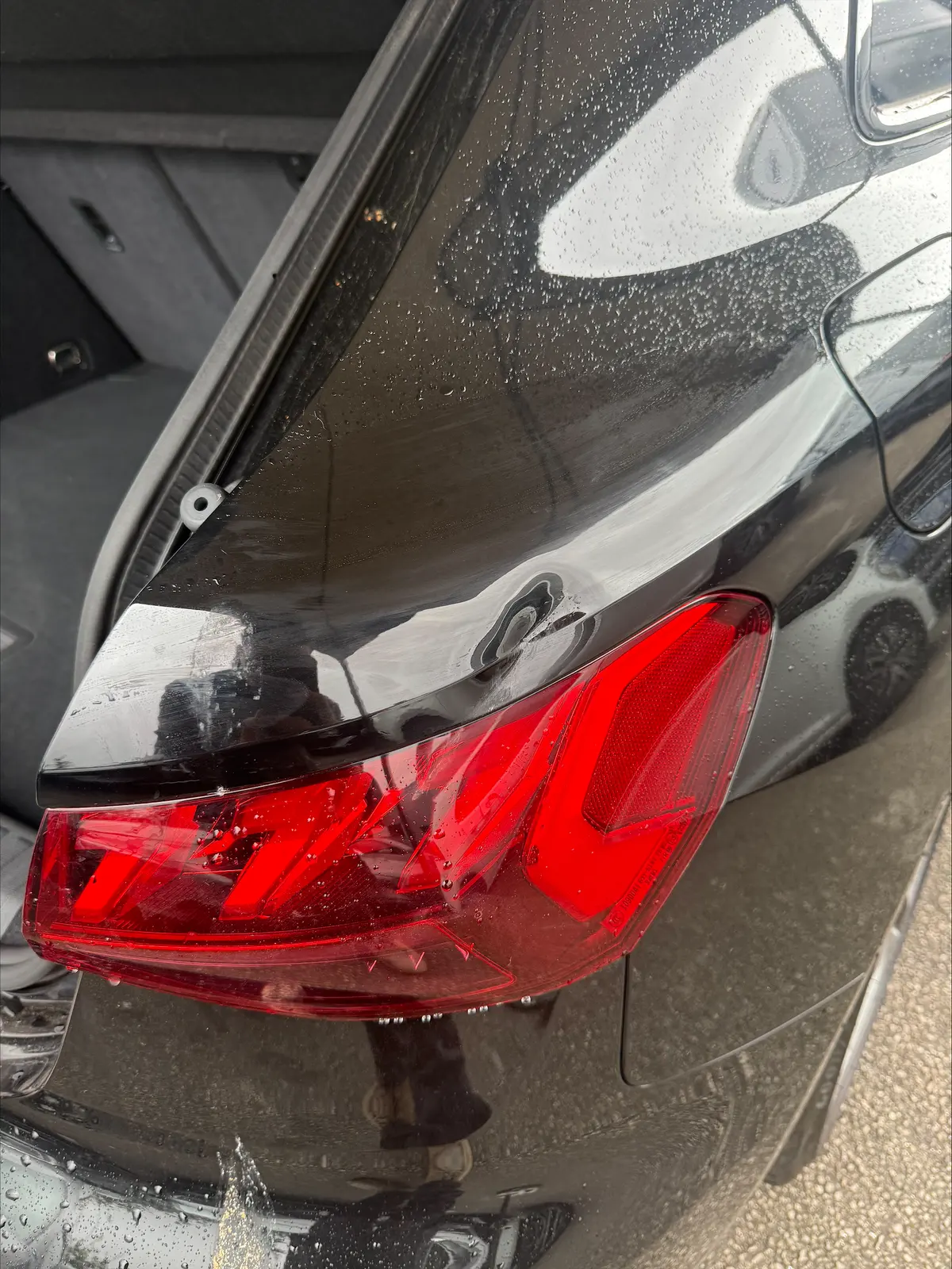Dent in a black car's rear quarter panel above the rear light, before repair