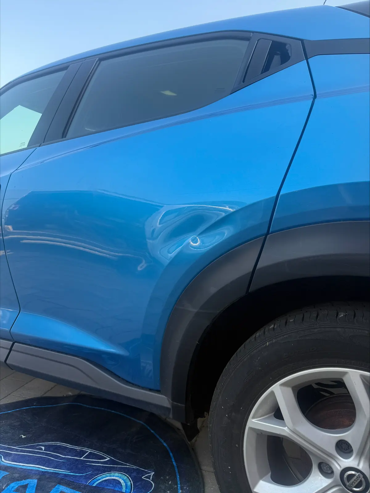 Dent in a blue car's rear quarter panel before repair